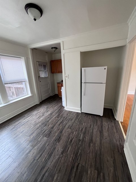 A room with a white fridge and wooden floors.